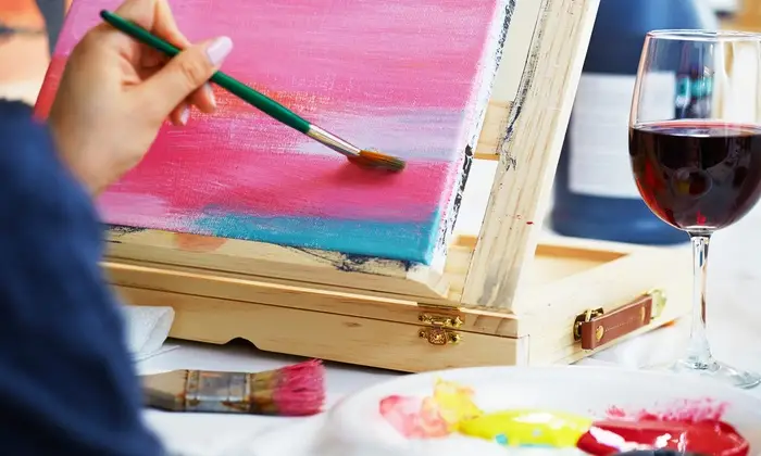 The picture depicts a man painting and a glass of wine
